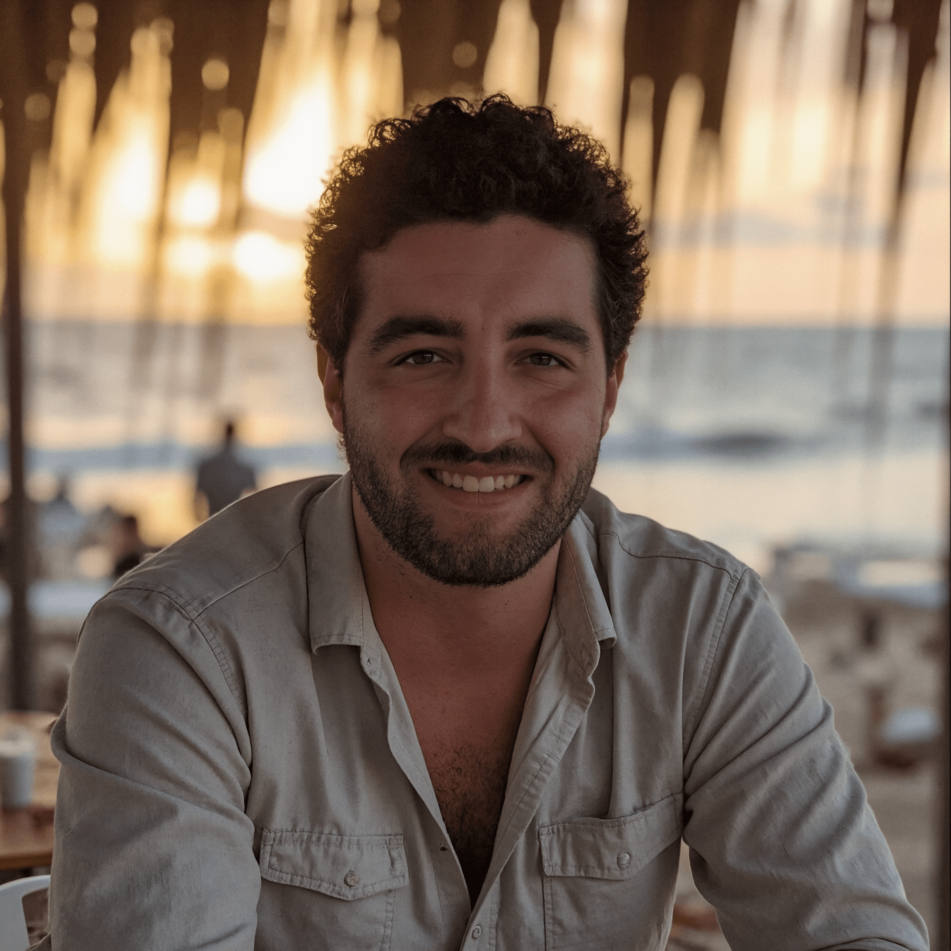 Me sitting at a table in front of the beach during sunset. I'm wearing a light shirt